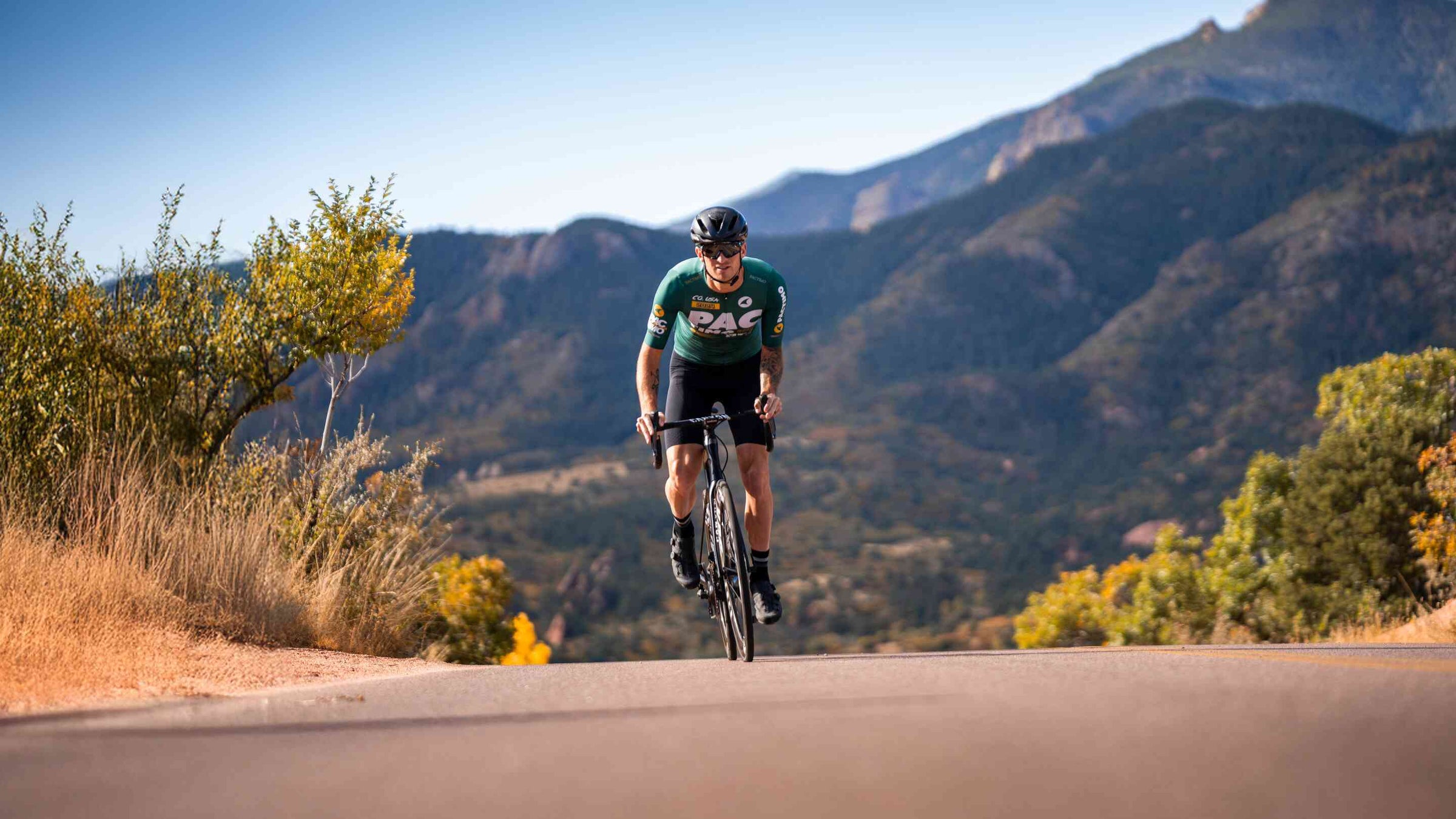 Cyclist in aerodynamic green cycling jersey and black bib shorts crests a hill while riding out of the saddle