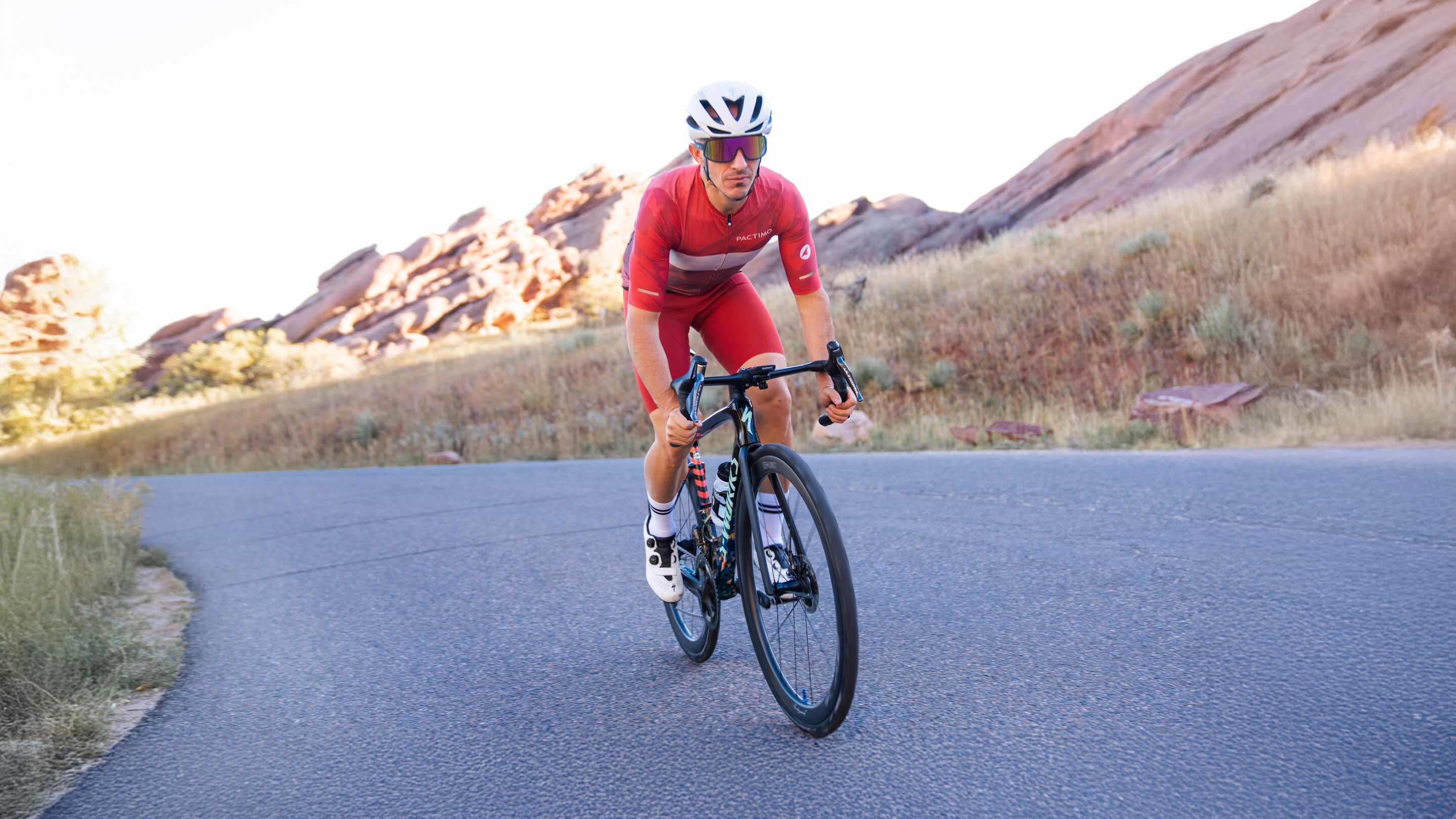 Cyclist wearing red cycling bib shorts and red cycling jersey with Red Rocks in background.