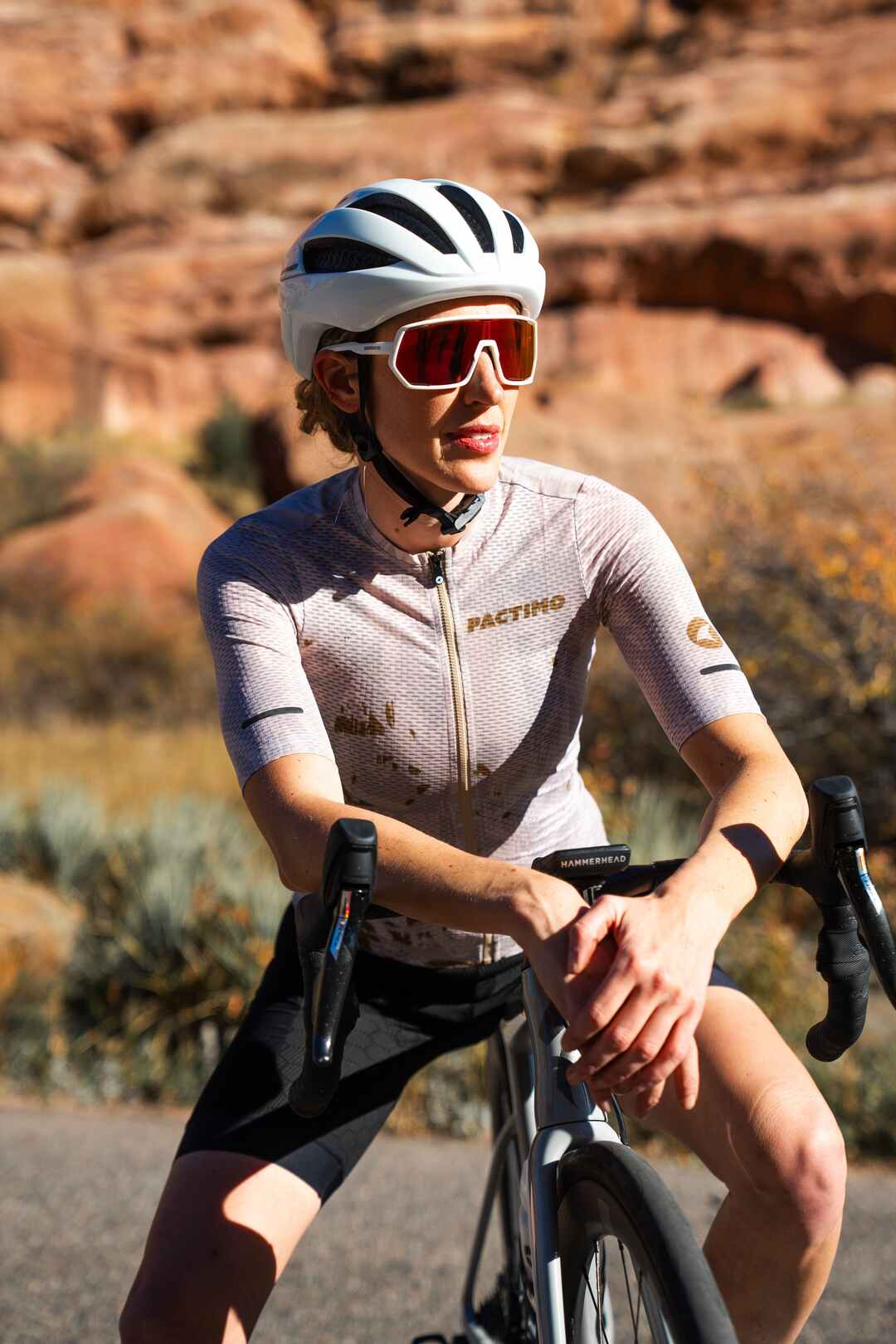 Female cyclist wearing a mesh sand colored cycling jersey with Red Rocks behind her