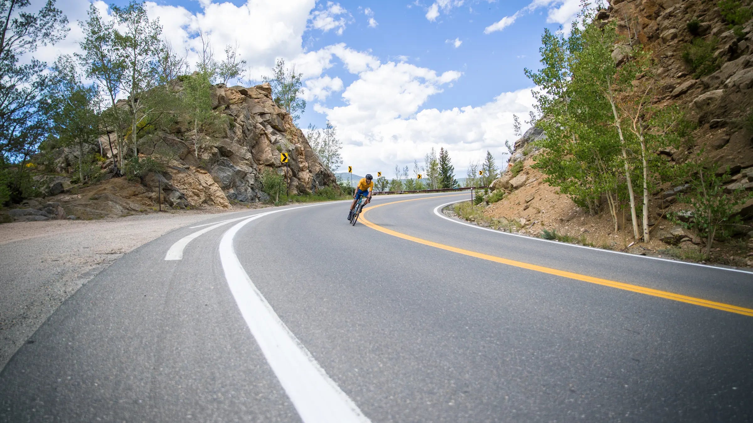 Cyclist descending a mountain pass with cloudy sky in the background