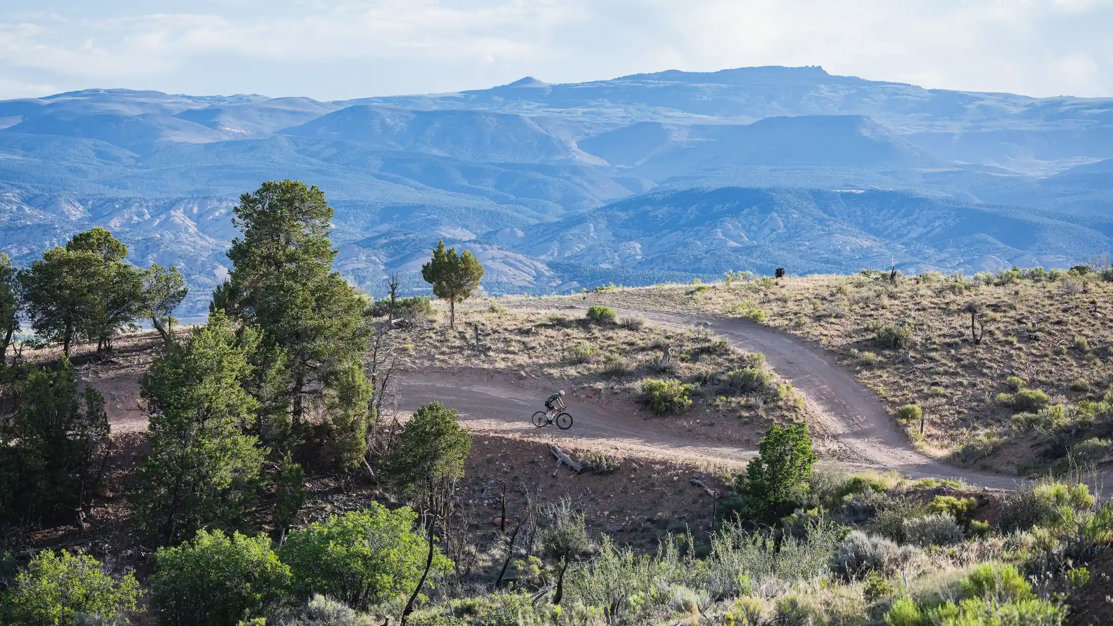 Lone cyclist on a dirt trail with rolling mountains in the background