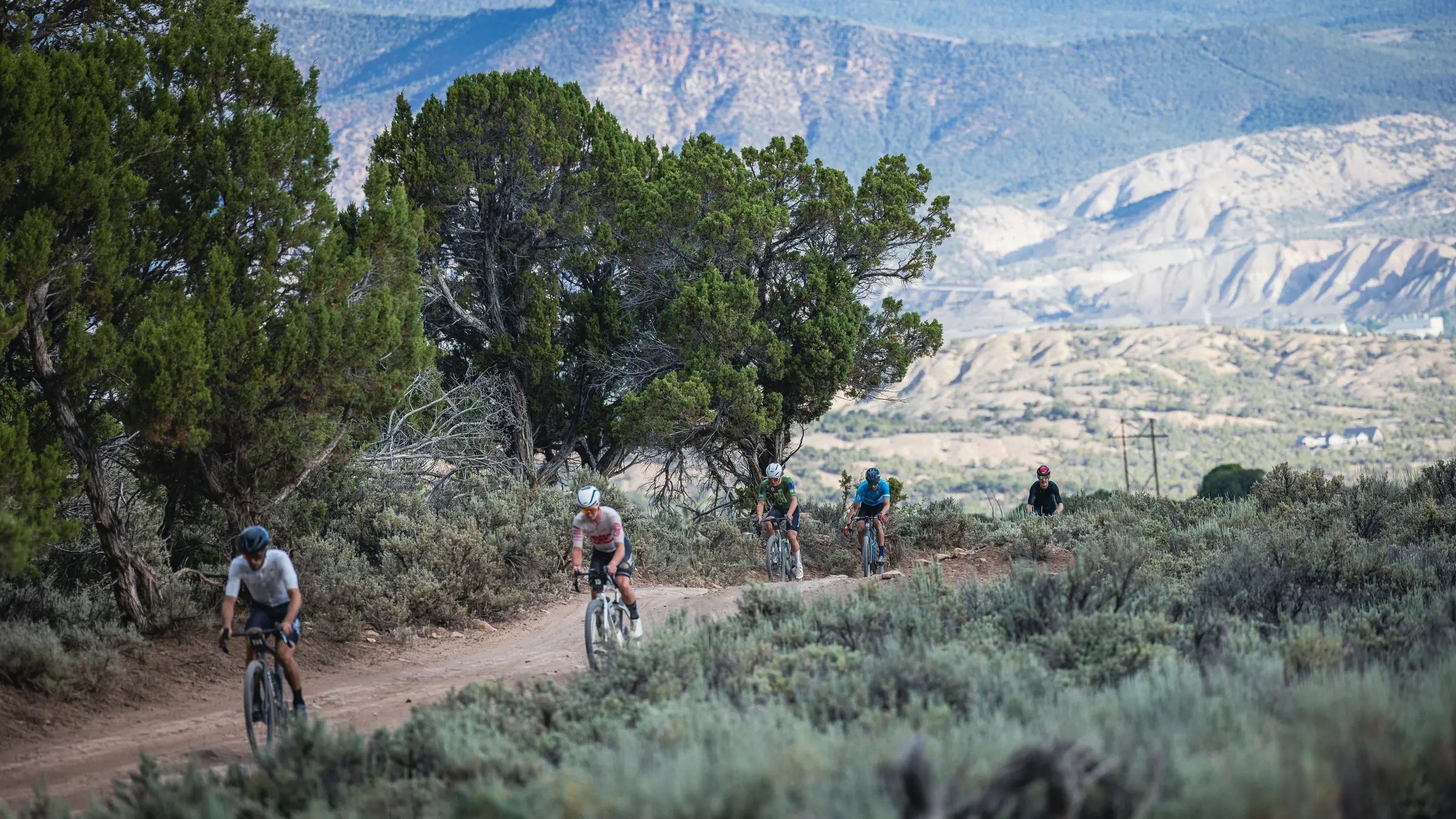 Group of cyclists riding on a dirt road with mountains in the background