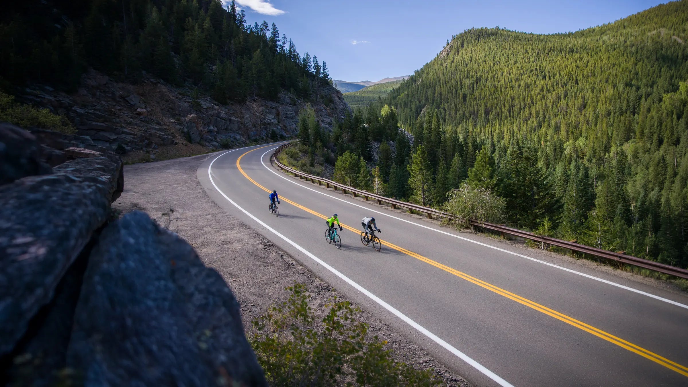 Three cyclist descending a mountain road with a valley and blue sky in the background