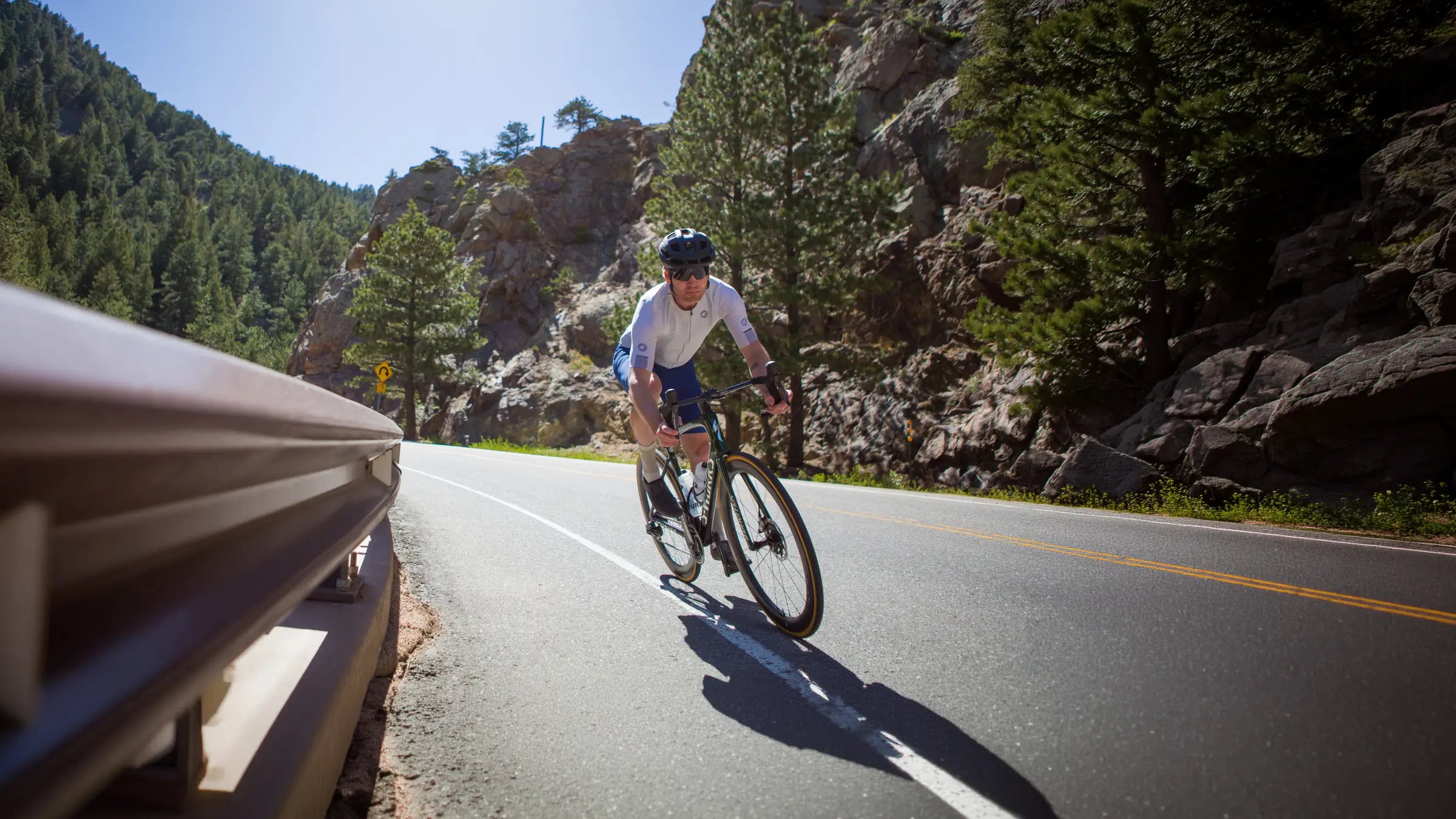 A male cyclist descending a road near the guard rail