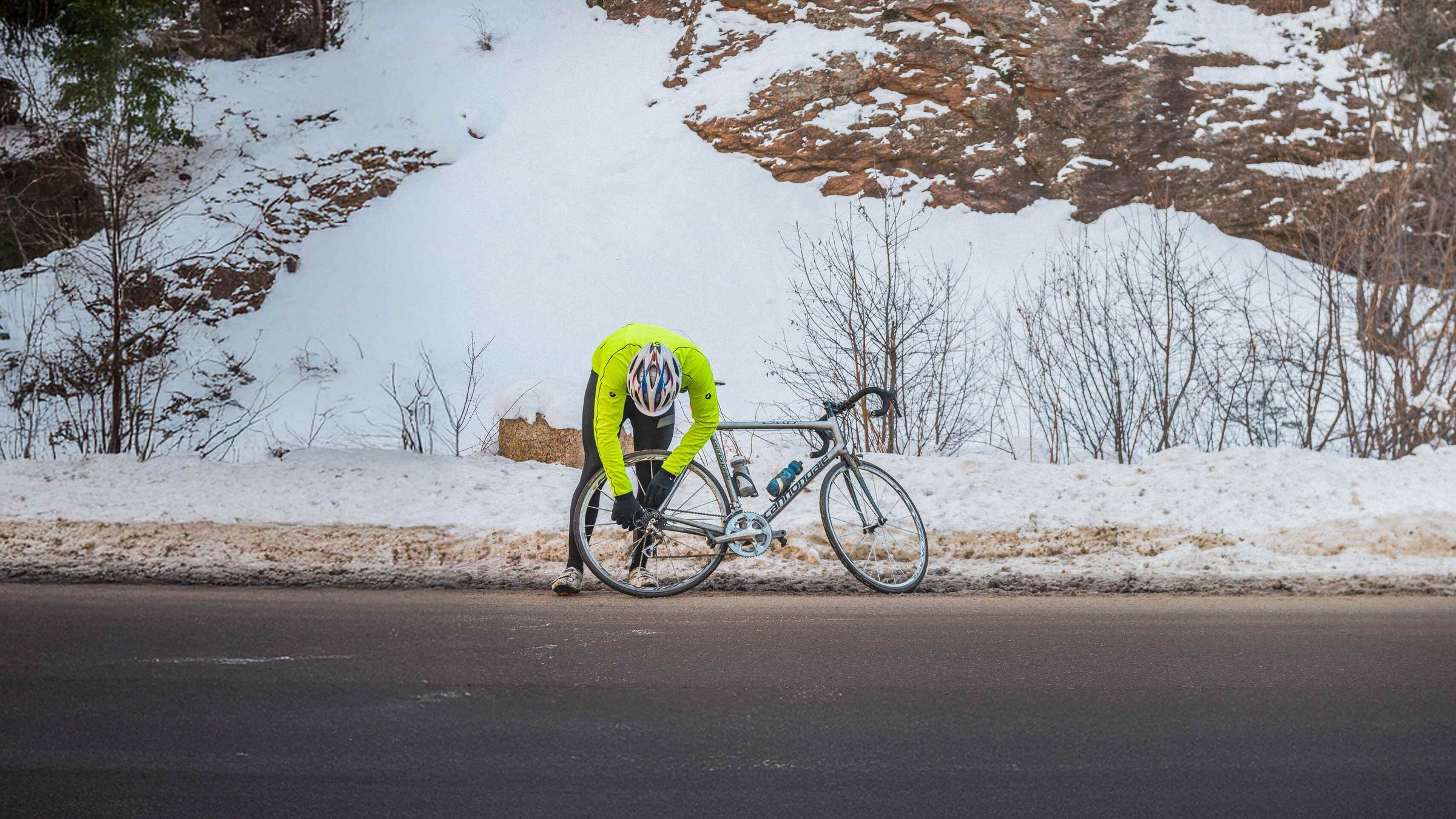 Cyclist in a bright yellow jacket with a bike on a snowy road