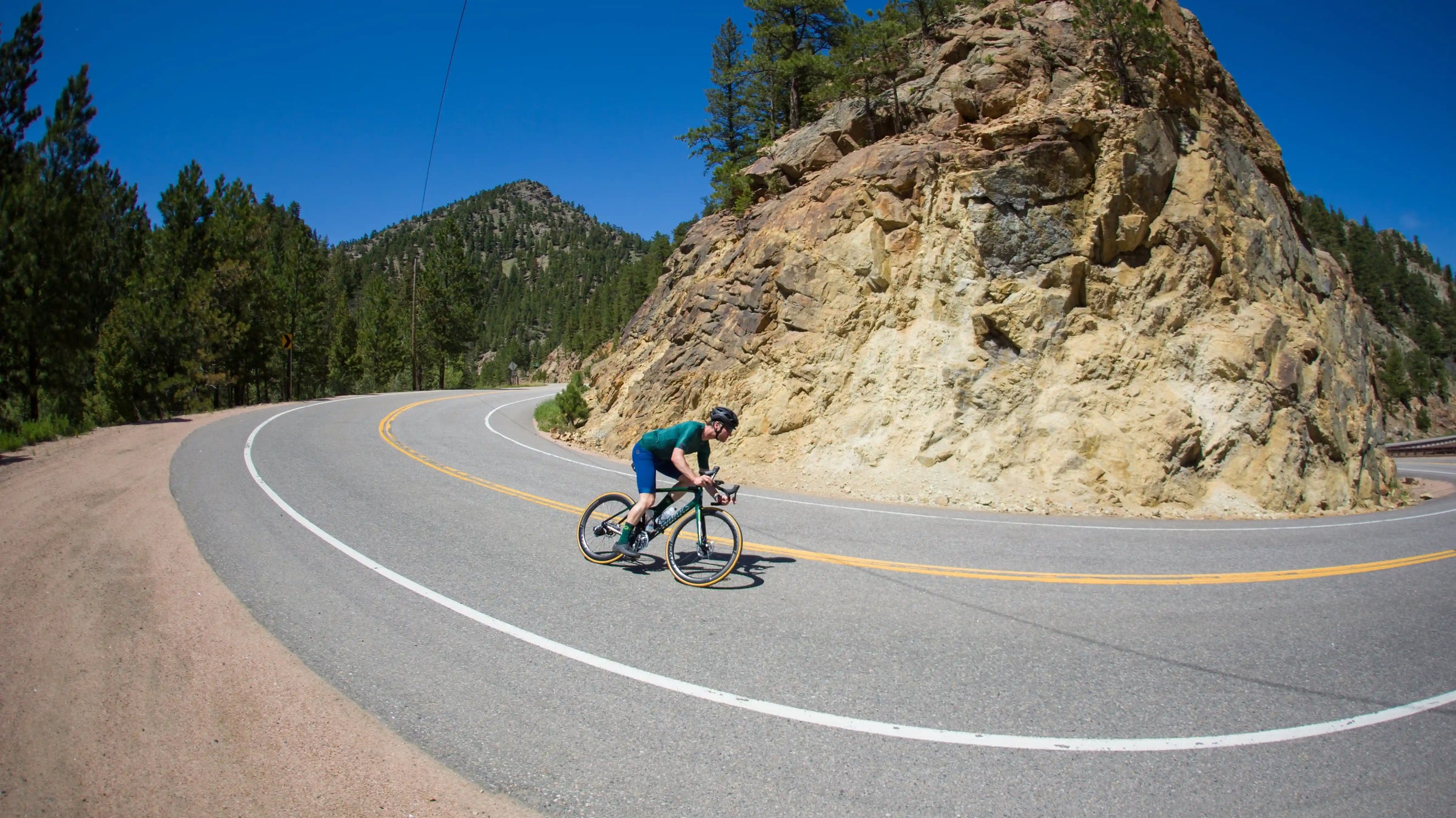 A male cyclist descending a sharp turn with rocky hills in the background