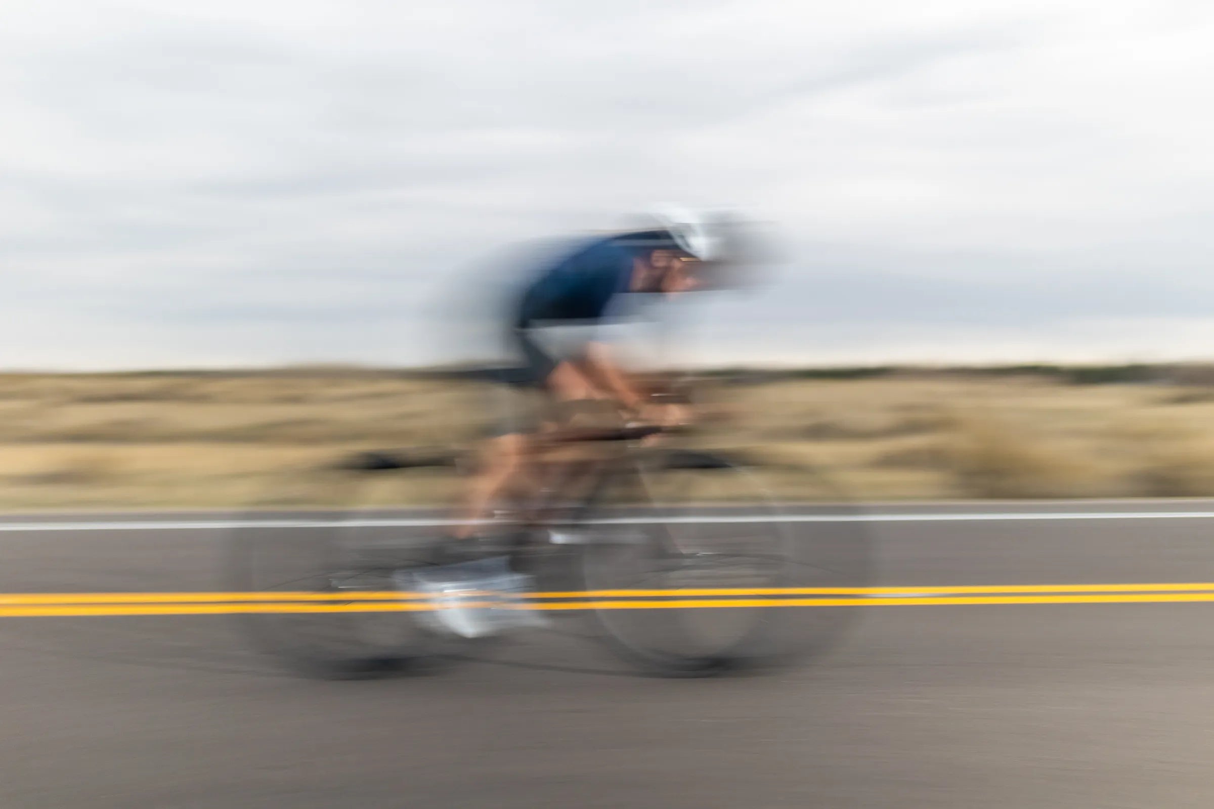 Blurry image of a cyclist riding very fast on a flat road