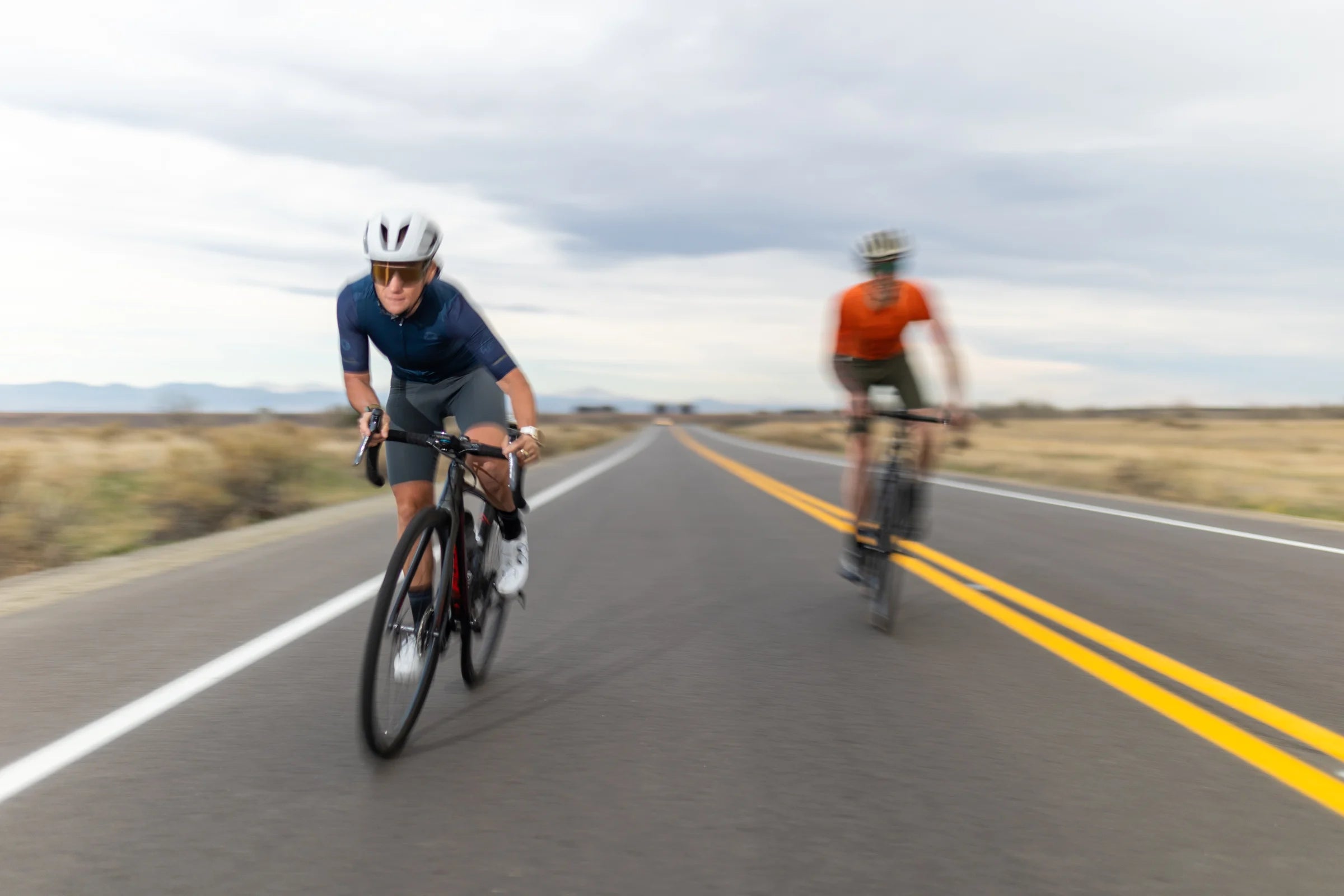 Two cyclist riding fast on a long flat road
