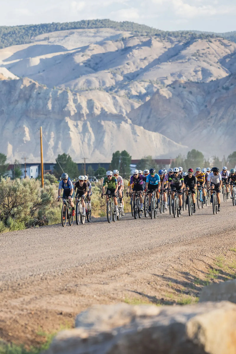 Group of cyclists competing in Bighorn Gravel on a dirt road with mountains in the background