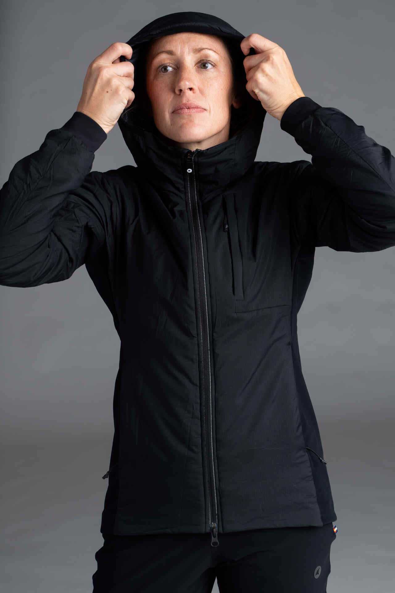 A woman putting on the hood of the Prologue Insulated Jacket